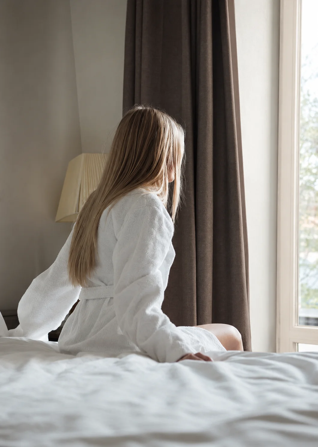Guest seated on a hotel bed looking out the window